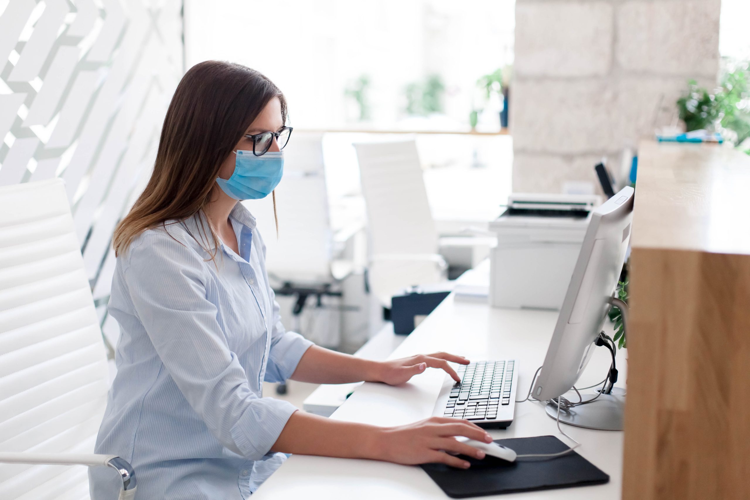 Young medical receptionist wearing a mask and working on a computer.